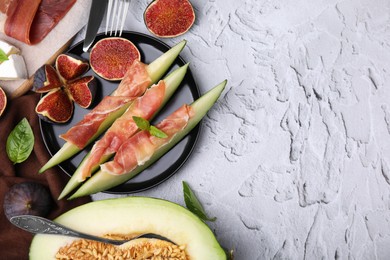 Photo of Tasty melon, jamon and figs served on white textured table, flat lay. Space for text
