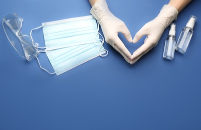 Photo of Person in gloves showing heart gesture surrounded by medical items on blue background, top view. Space for text