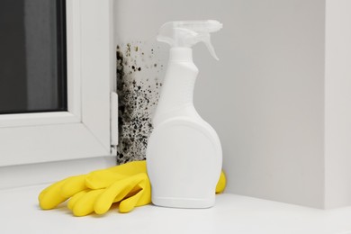 Image of Mold remover spray bottle and rubber gloves near affected window slope in room