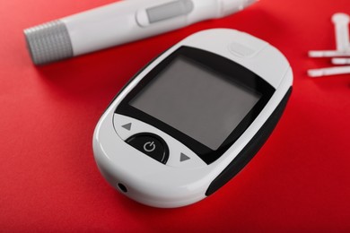 Photo of Digital glucometer, lancets and pen on red background. Diabetes control