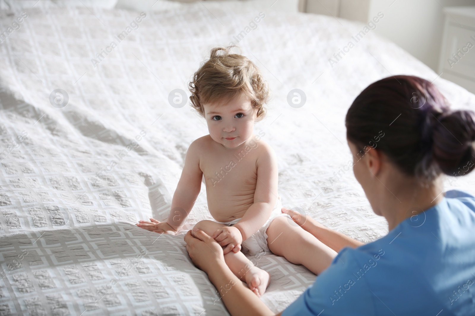 Photo of Orthopedist examining cute little baby on bed