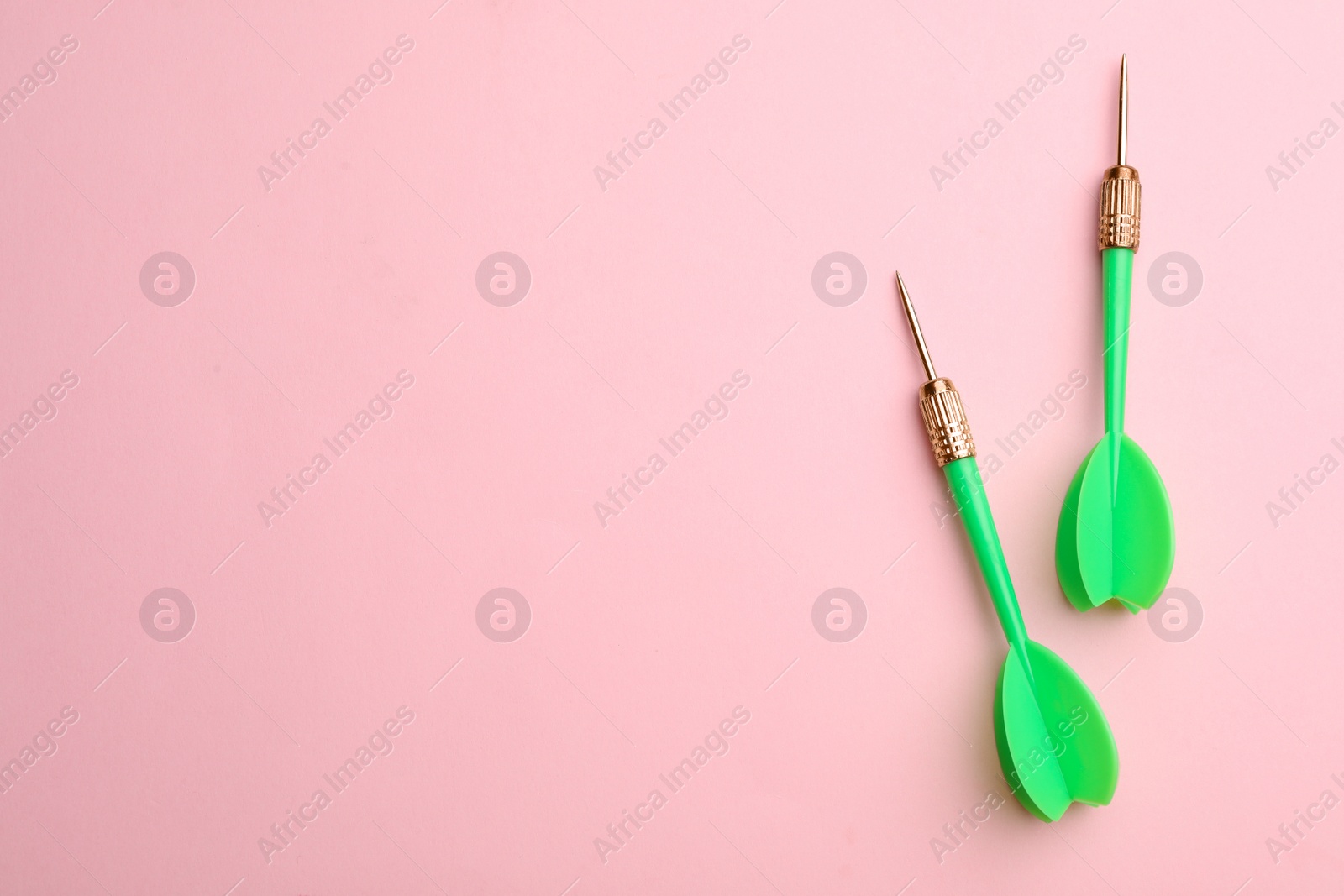 Photo of Green dart arrows on pink background, flat lay with space for text