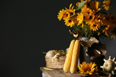 Photo of Beautiful autumn bouquet, corn cobs and small pumpkins on wooden table against dark grey background. Space for text