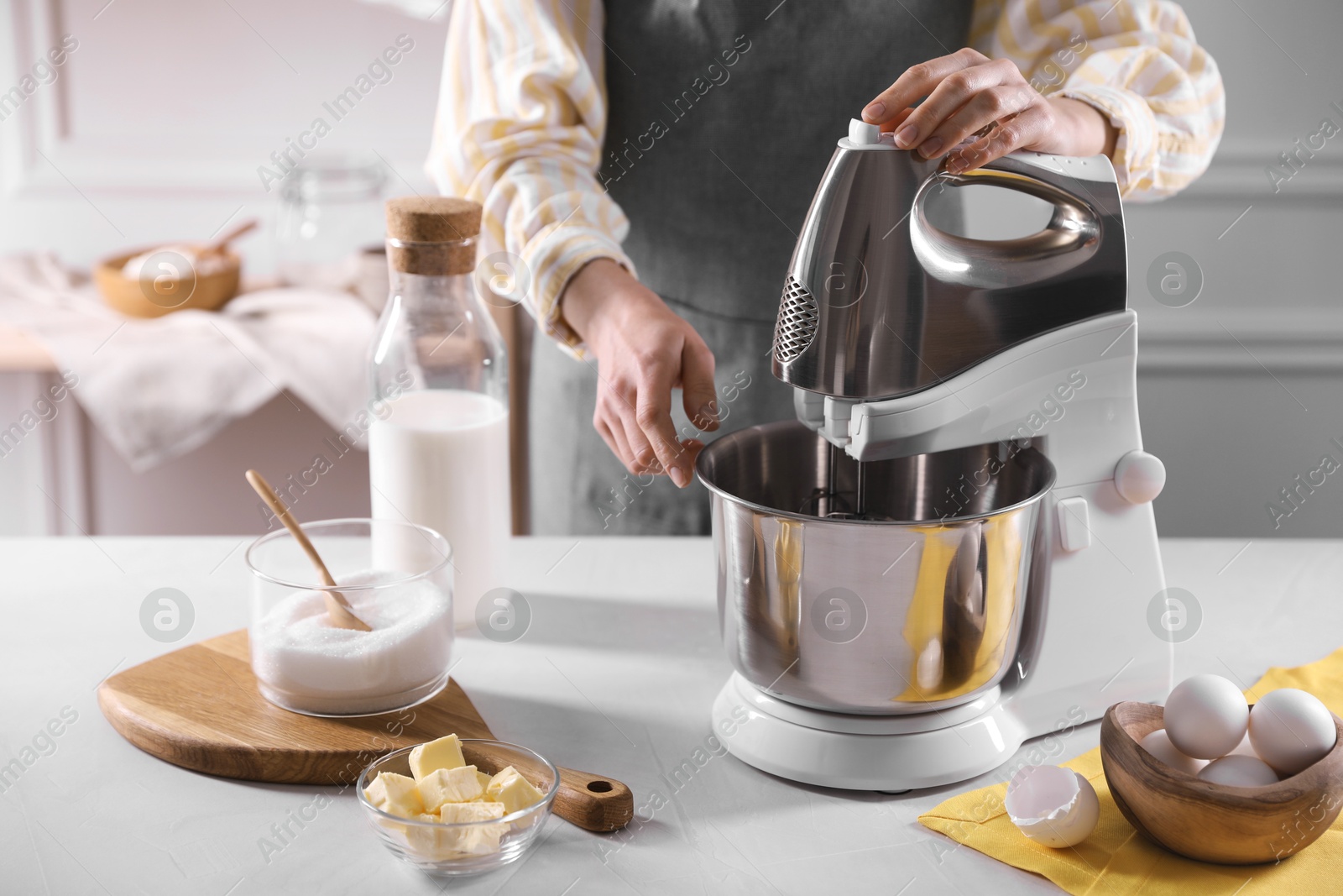 Photo of Woman making dough with stand mixer at table, closeup