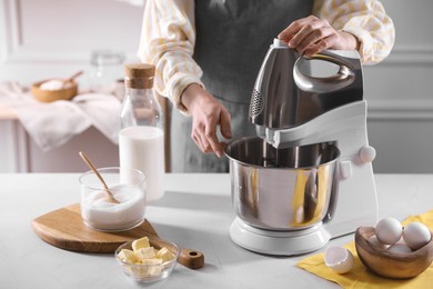 Woman making dough with stand mixer at table, closeup