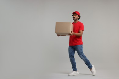 Happy young courier with parcel on grey background, space for text
