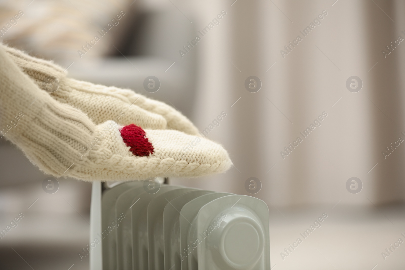 Photo of Woman in mittens warming hands on electric heater at home, closeup. Space for text