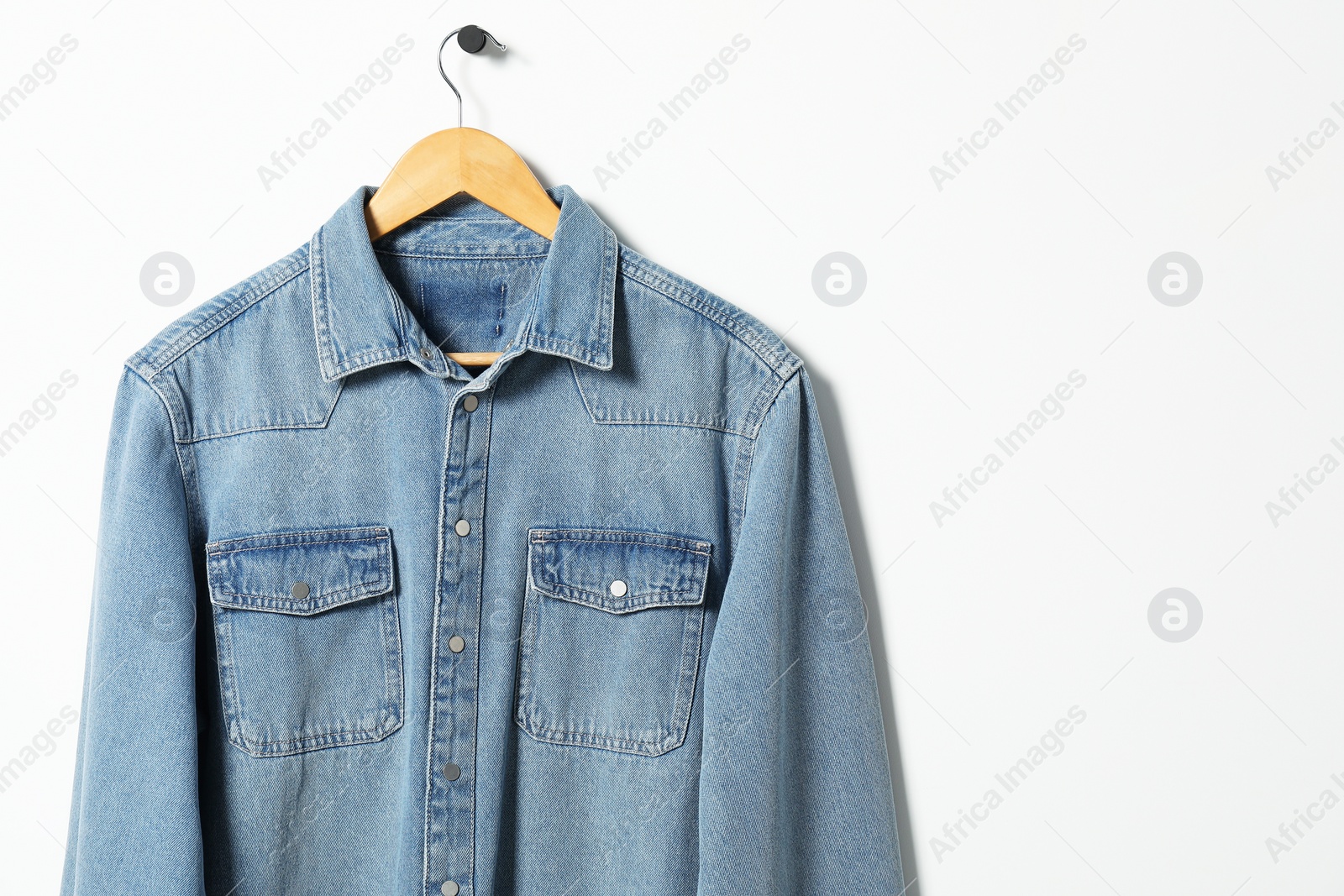 Photo of Hanger with denim shirt on white wall, space for text