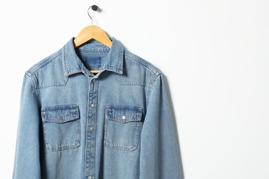 Photo of Hanger with denim shirt on white wall, space for text
