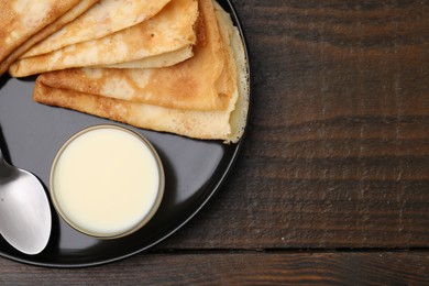 Photo of Tasty condensed milk and crepes on wooden table, top view. Space for text