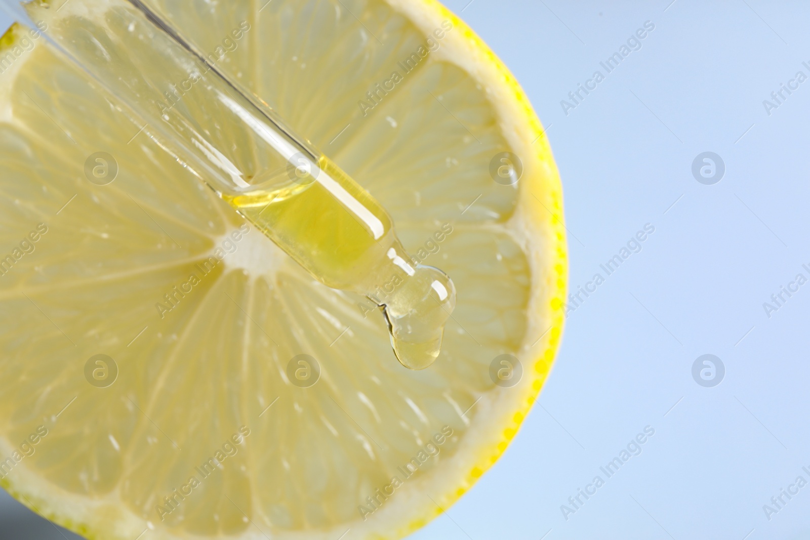 Photo of Dripping cosmetic serum from pipette onto lemon slice against light blue background, closeup. Space for text