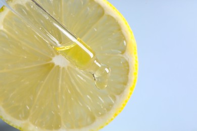 Photo of Dripping cosmetic serum from pipette onto lemon slice against light blue background, closeup. Space for text
