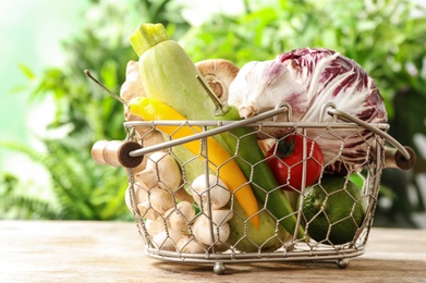 Photo of Fresh vegetables in metal basket on wooden table against blurred green background