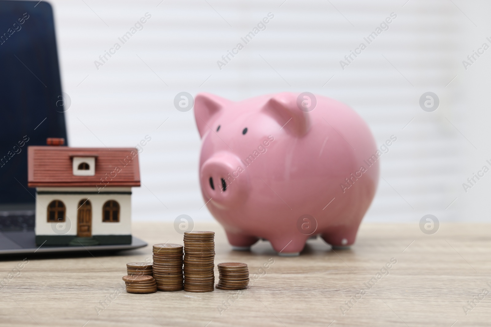 Photo of House model, piggy bank and stacked coins on light wooden table, selective focus