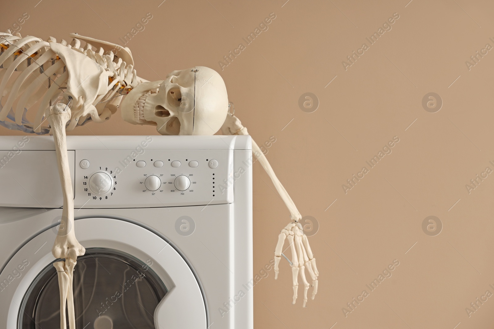 Photo of Waiting concept. Human skeleton lying on washing machine near beige wall indoors, space for text