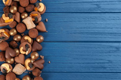 Different delicious chocolate candies on blue wooden table, flat lay. Space for text