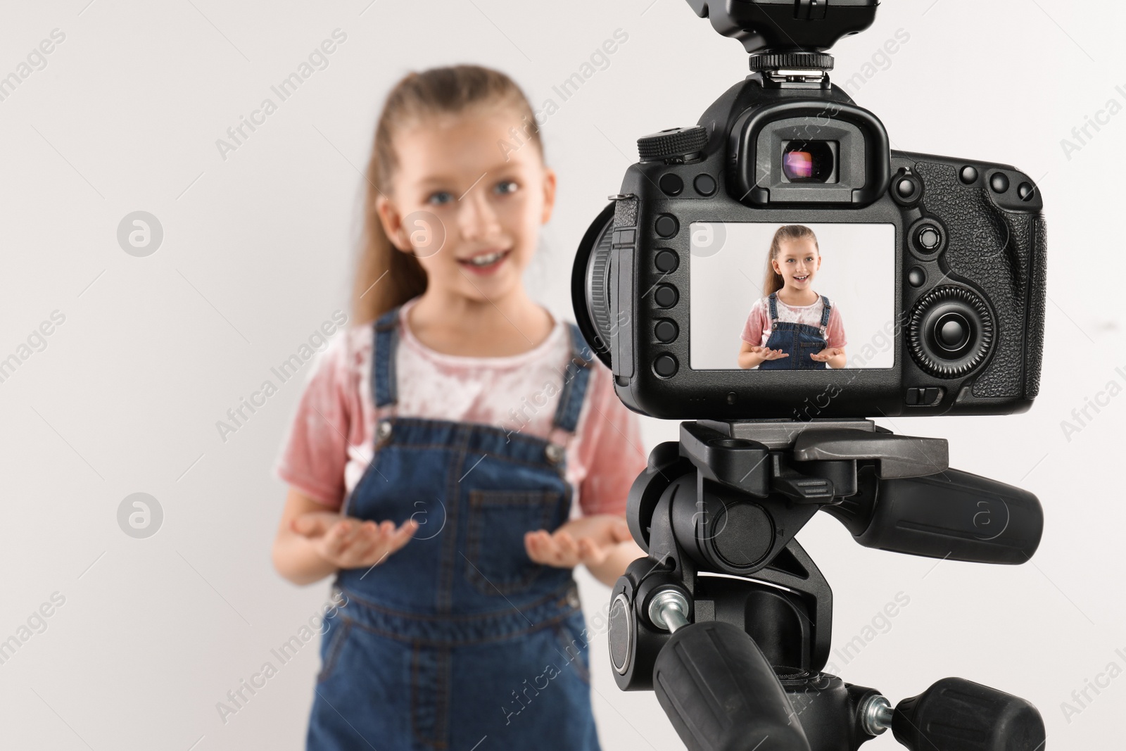 Photo of Cute little blogger recording video against white background, focus on camera