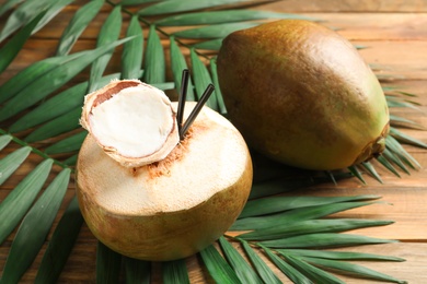Photo of Fresh green coconuts and palm leaves on wooden table