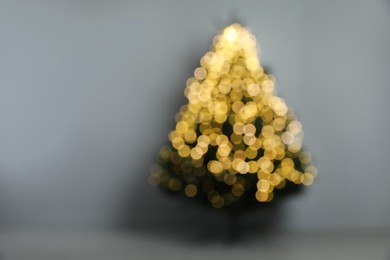 Photo of Blurred view of beautiful fir tree with Christmas lights  near grey wall in room, space for text
