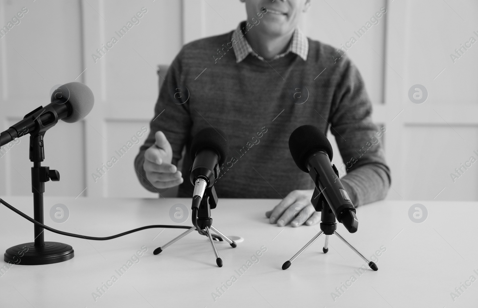 Image of Journalist conference. Man giving interview at table with microphones indoors, closeup. Black and white effect