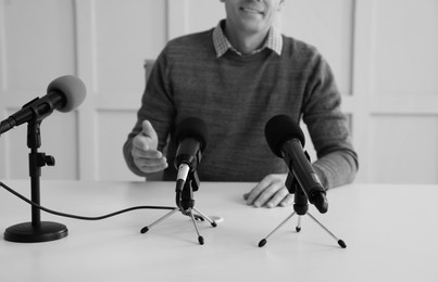 Image of Journalist conference. Man giving interview at table with microphones indoors, closeup. Black and white effect