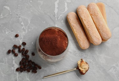 Photo of Tasty tiramisu in glass, coffee beans, spoon and biscuits on light grey table, flat lay