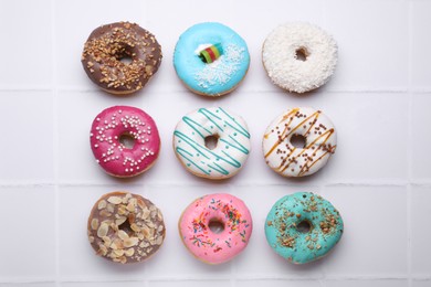 Different tasty donuts on white tiled table, flat lay
