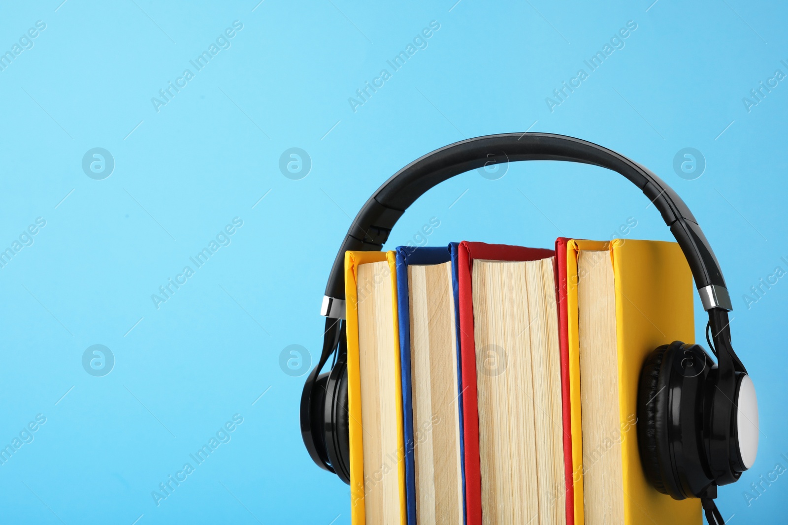 Photo of Books and modern headphones on light blue background. Space for text