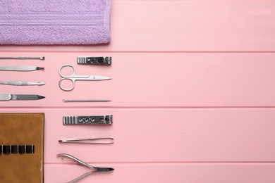 Set of manicure tools, towel and case on pink wooden background, flat lay. Space for text