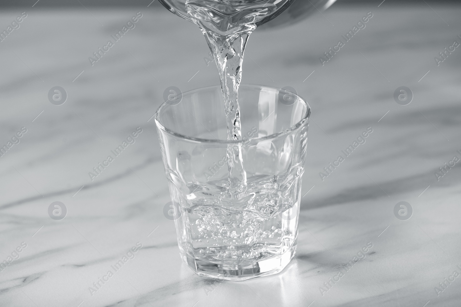 Photo of Pouring water into glass on white marble table, closeup