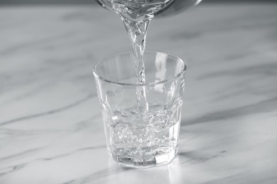 Photo of Pouring water into glass on white marble table, closeup