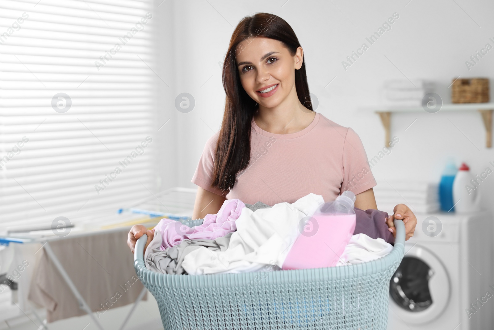 Photo of Woman holding basket with dirty clothes and fabric softener in bathroom, space for text