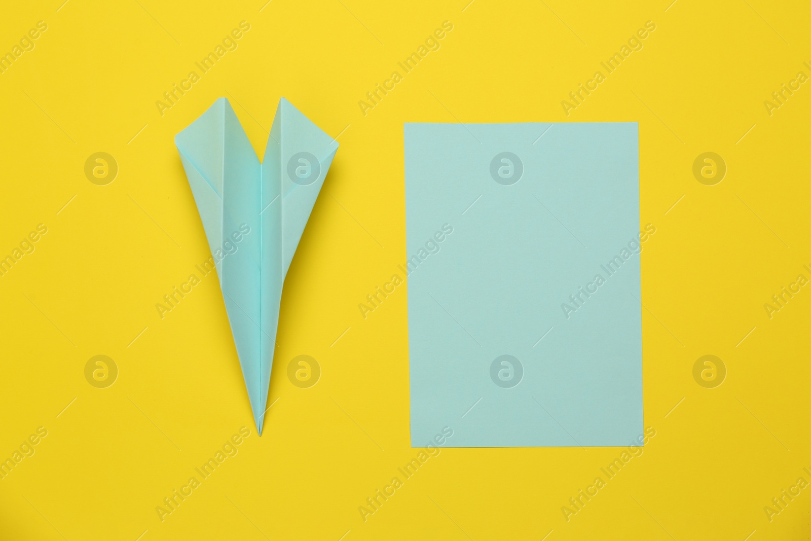 Photo of Handmade light blue plane and piece of paper on yellow background, flat lay