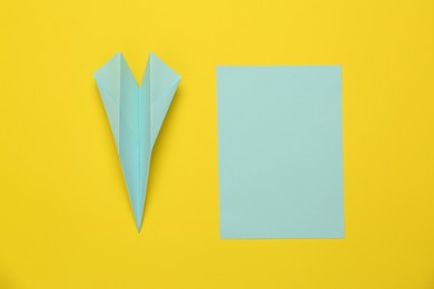 Photo of Handmade light blue plane and piece of paper on yellow background, flat lay