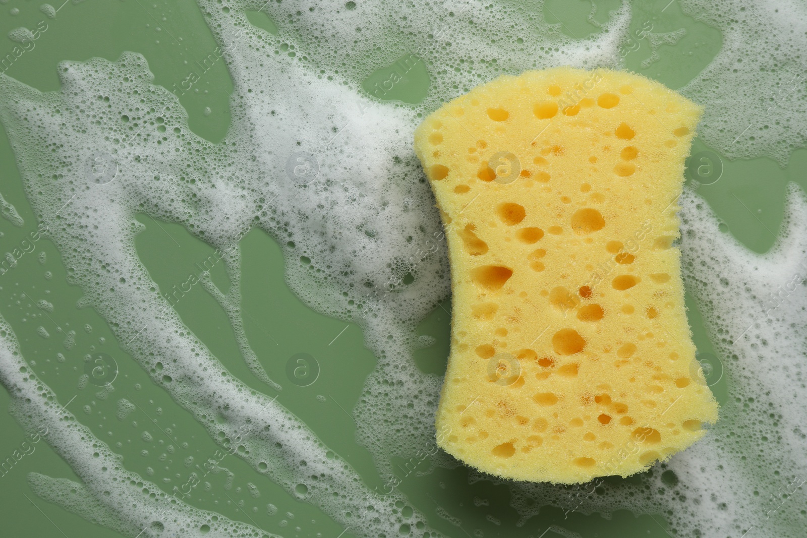 Photo of Yellow sponge with foam on green background, top view