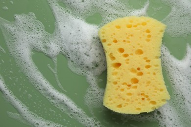 Yellow sponge with foam on green background, top view