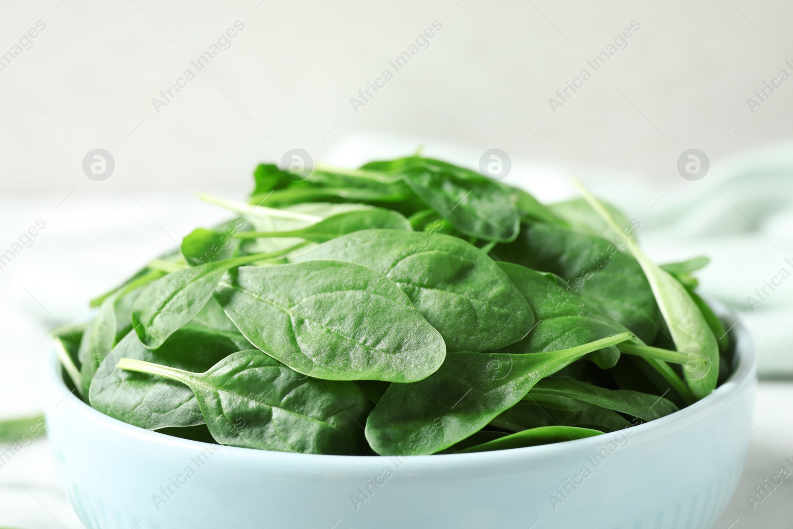 Photo of Bowl of fresh green healthy spinach on table, closeup