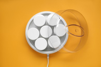 Photo of Modern yogurt maker with jars on orange background, top view