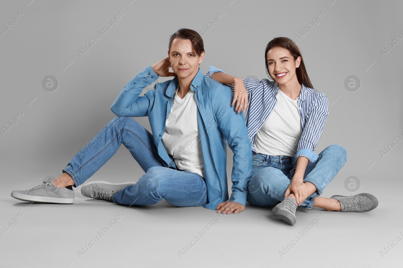 Photo of Young couple in stylish jeans sitting on grey background