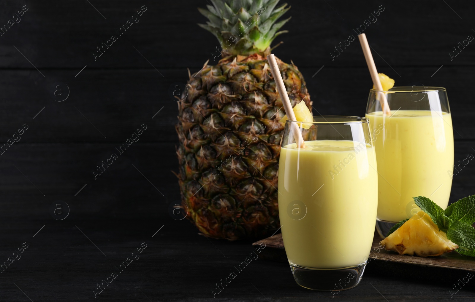 Photo of Tasty pineapple smoothie and fruit on black table. Space for text