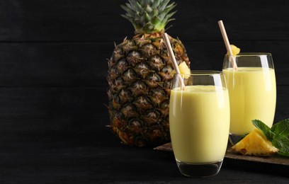 Photo of Tasty pineapple smoothie and fruit on black table. Space for text