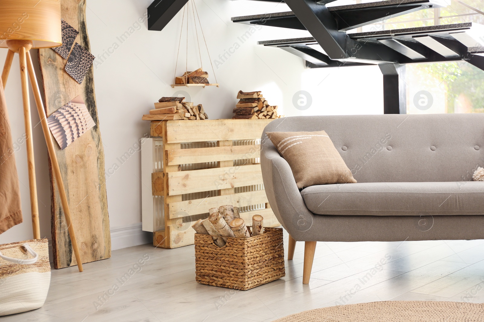 Photo of Basket with firewood near sofa indoors. Interior design