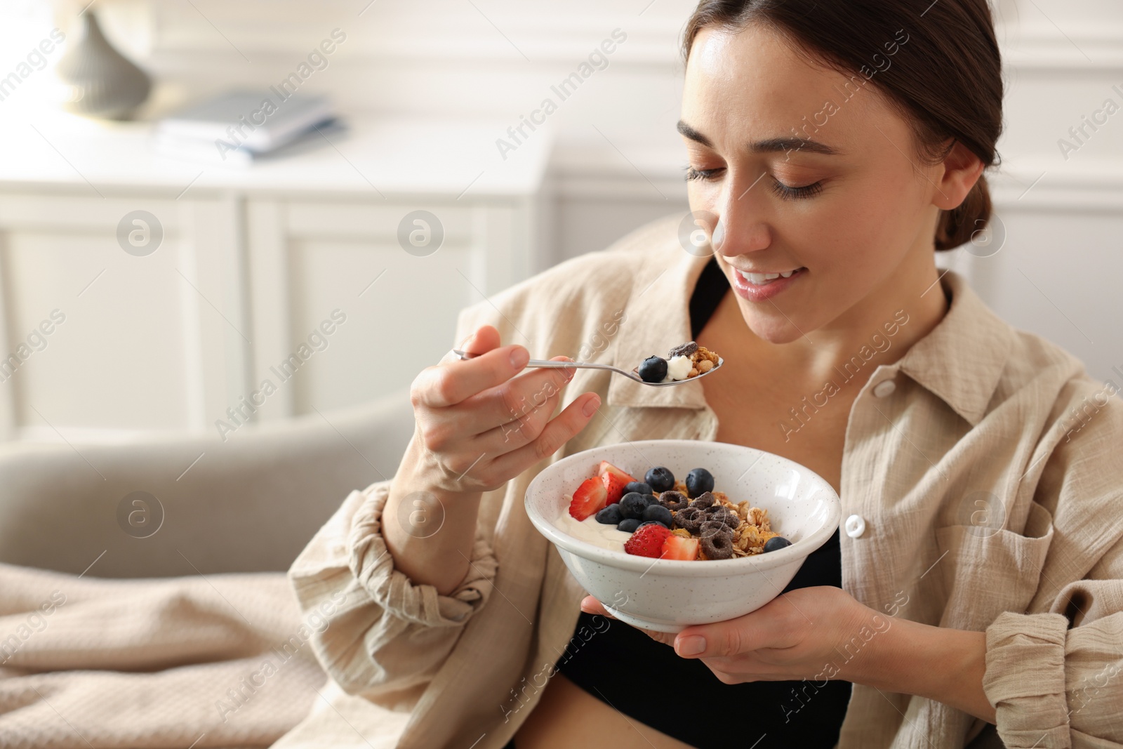 Photo of Woman eating tasty granola with fresh berries and yogurt at home