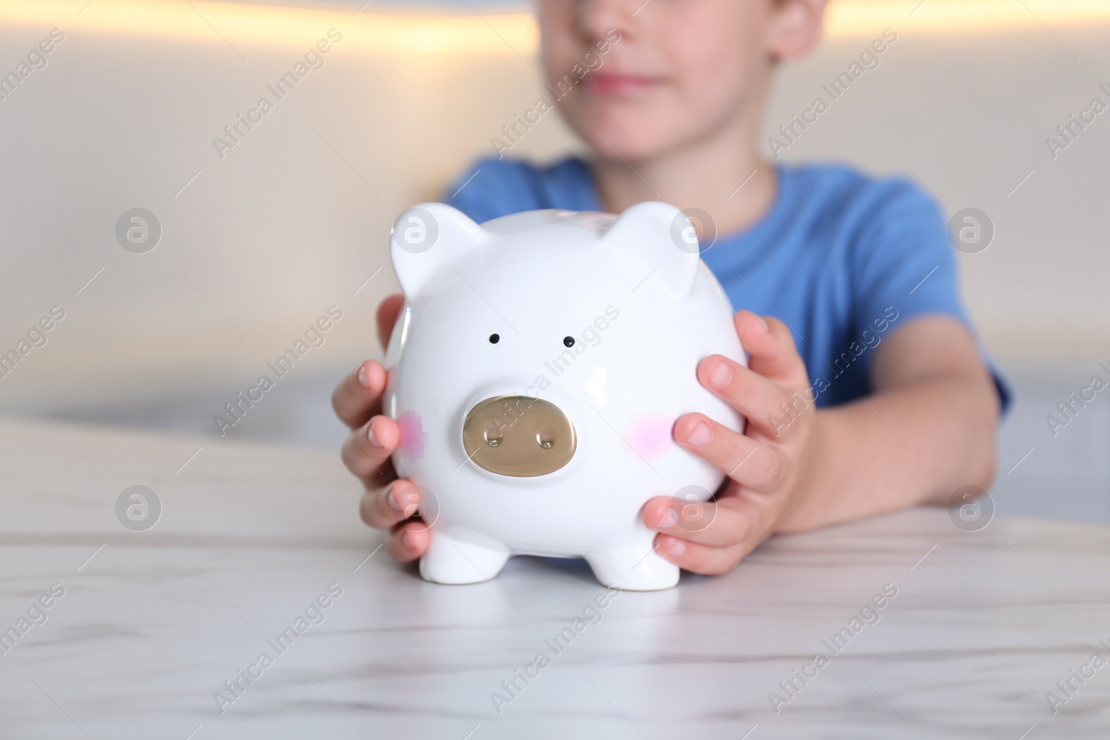 Photo of Little boy with piggy bank at marble table indoors, closeup
