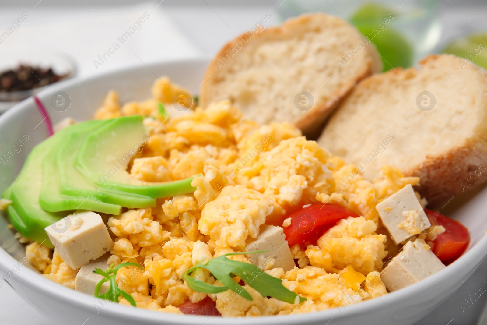 Photo of Bowl with delicious scrambled eggs, tofu and slices of baguette, closeup