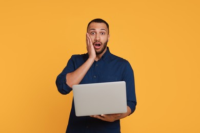Photo of Surprised young man with laptop on yellow background