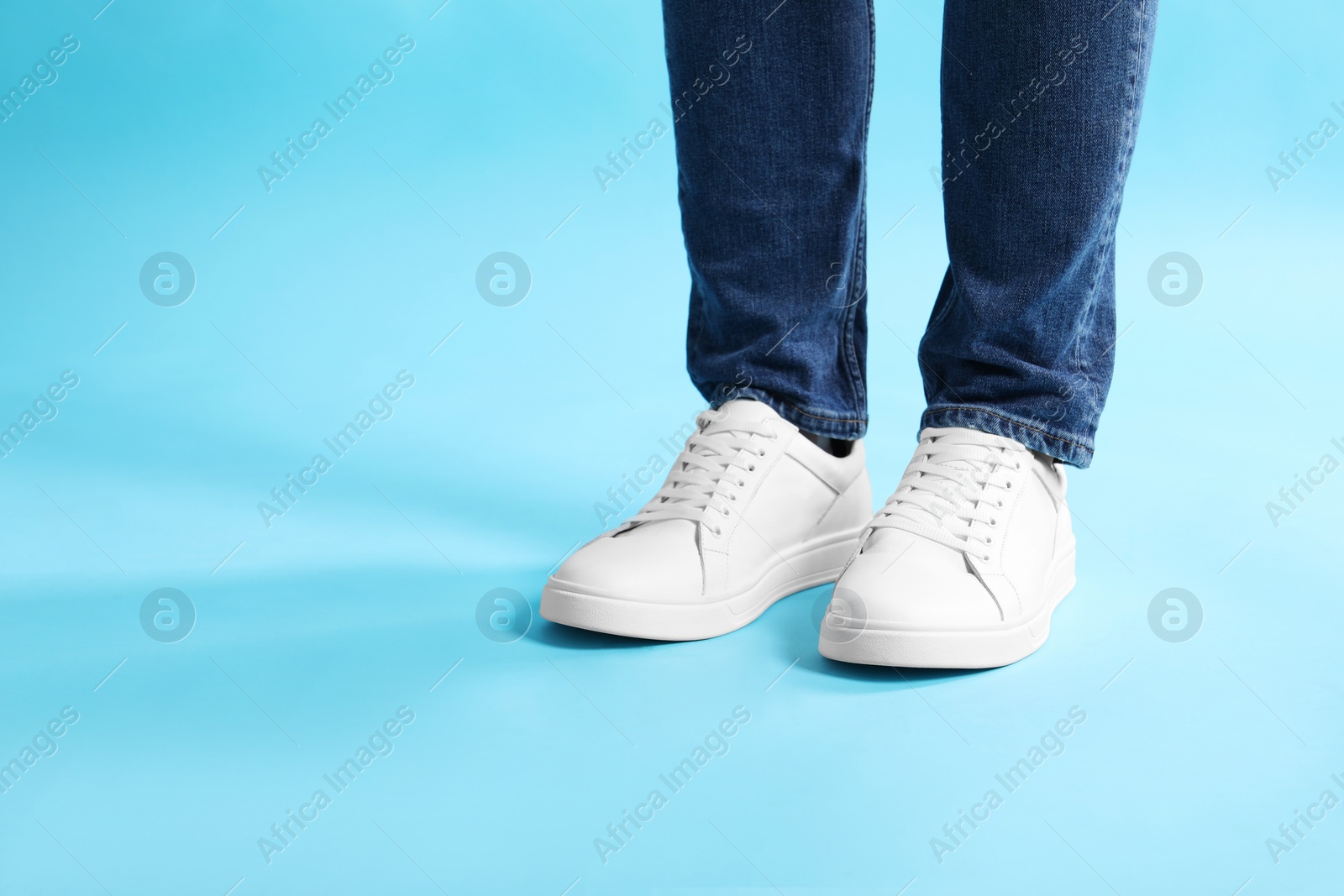 Photo of Man wearing stylish white sneakers on light blue background, closeup