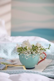 Beautiful bright flowers in cup and tray on bed