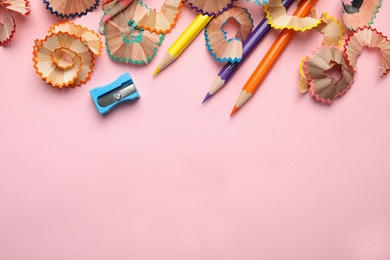 Photo of Color pencils, sharpener and shavings on pink background, top view. Space for text