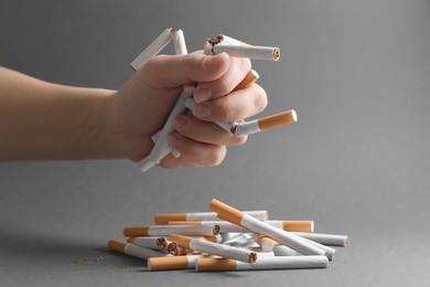 Stop smoking. Woman holding broken cigarettes over pile on grey background, closeup